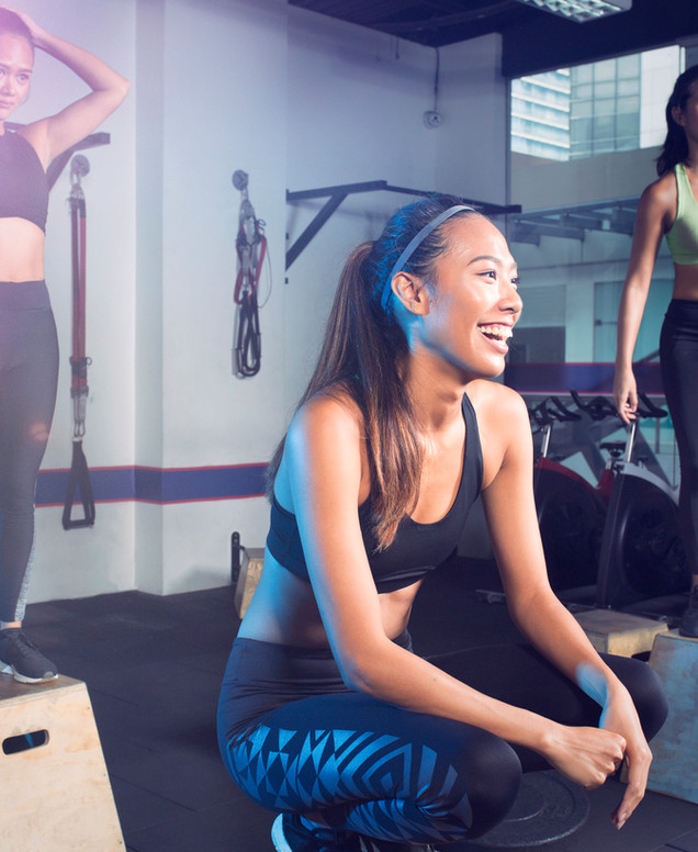 Lächelnde Frau in Sportkleidung hockt zwischen Trainingsboxen im Fitnessstudio