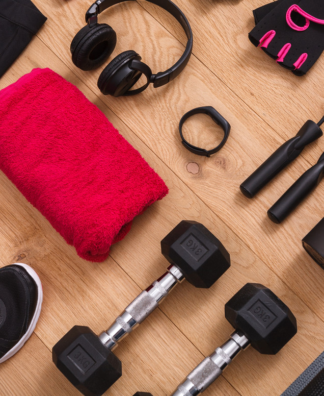 Kurzhanteln, Kopfhörer, Fitnessarmband und Trainingshandschuhe auf einem Holzboden